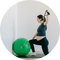 Pregnant woman exercising with a green ball and resistance band.