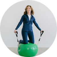 Woman balancing on a green balance ball with handles against a white background