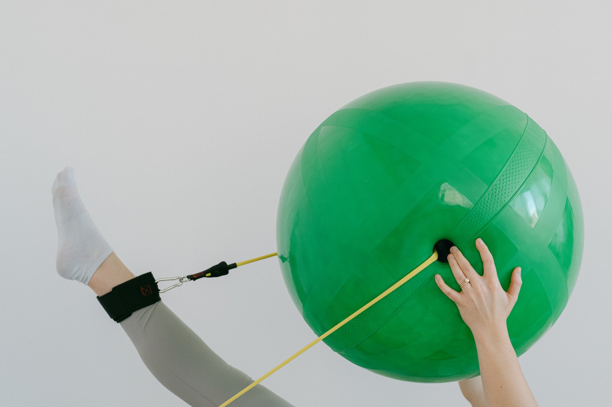Person using a green exercise ball with resistance bands on a plain background