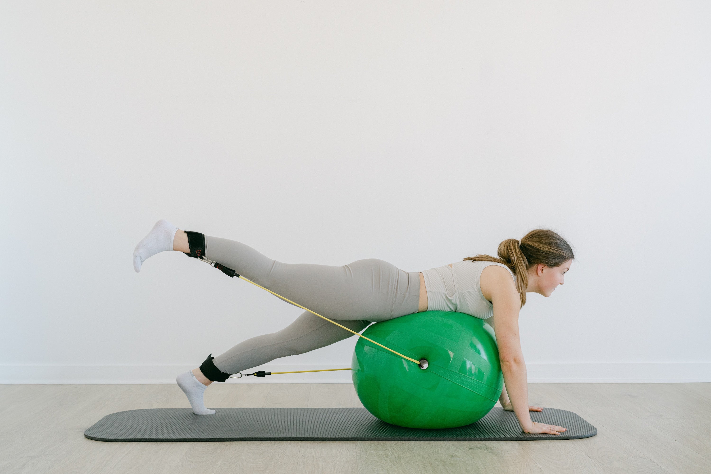 Woman exercising with a green stability ball and resistance band on a white background