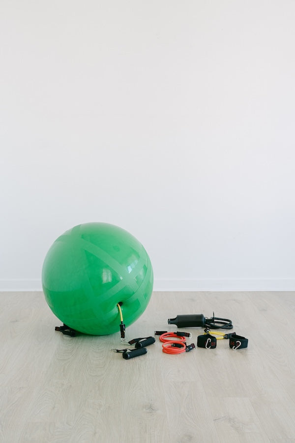Green exercise ball with resistance bands on a gray wooden floor against a white wall