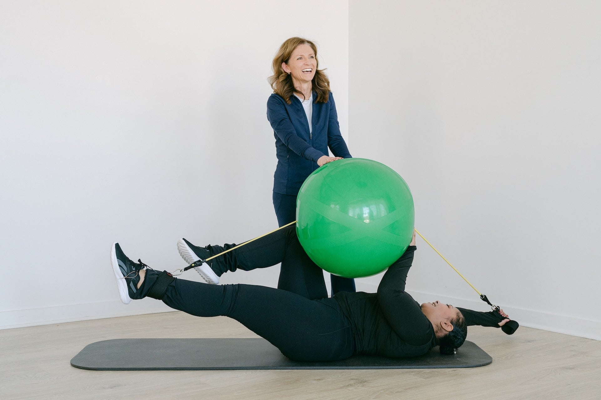 Person exercising with a green ball and resistance band, assisted by another person.