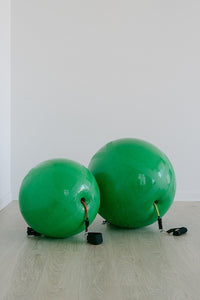 Two green exercise balls on a light wooden floor with a white wall background.