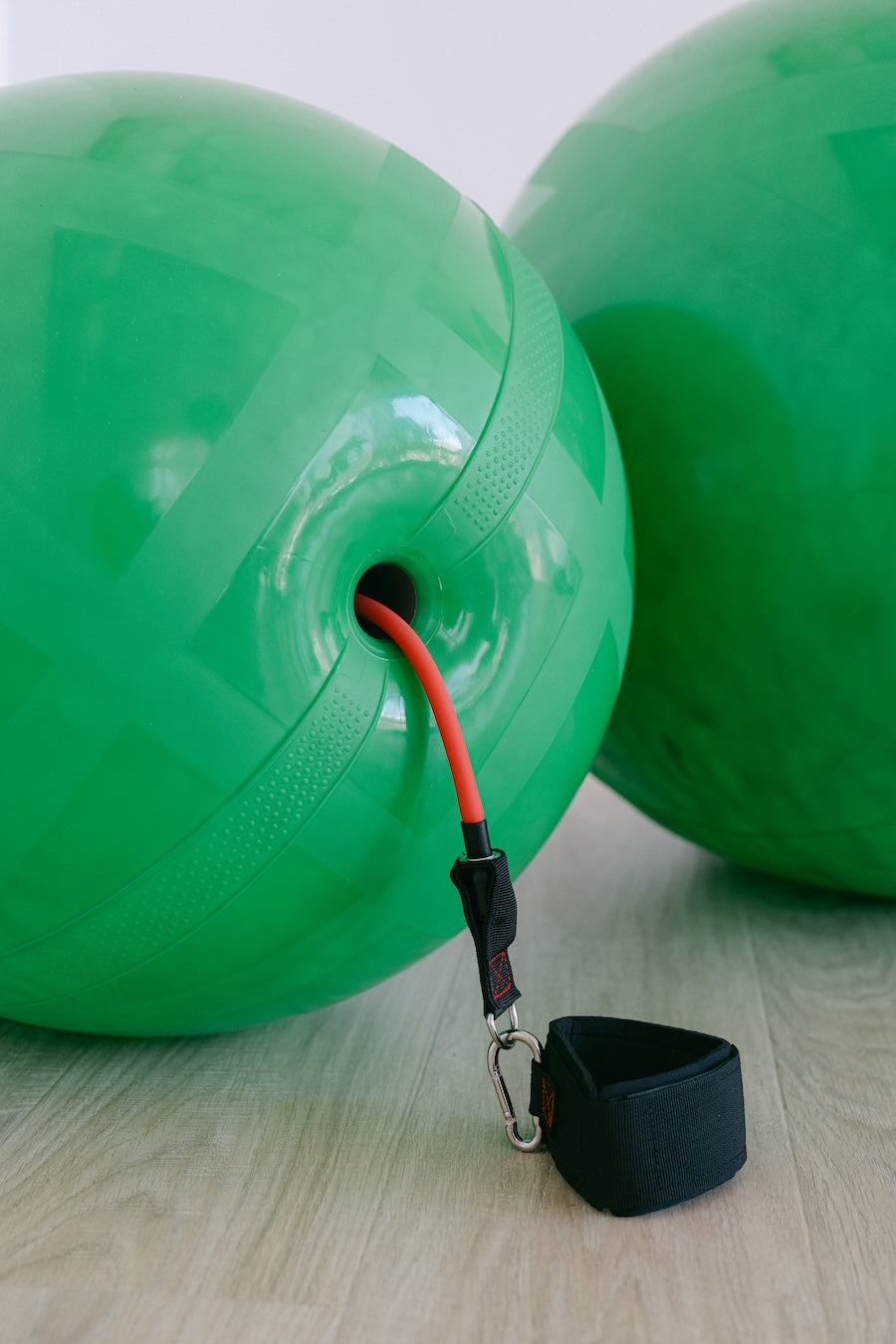 Green Chabu channel ball with a red resistance band and black strap on a light wooden floor.