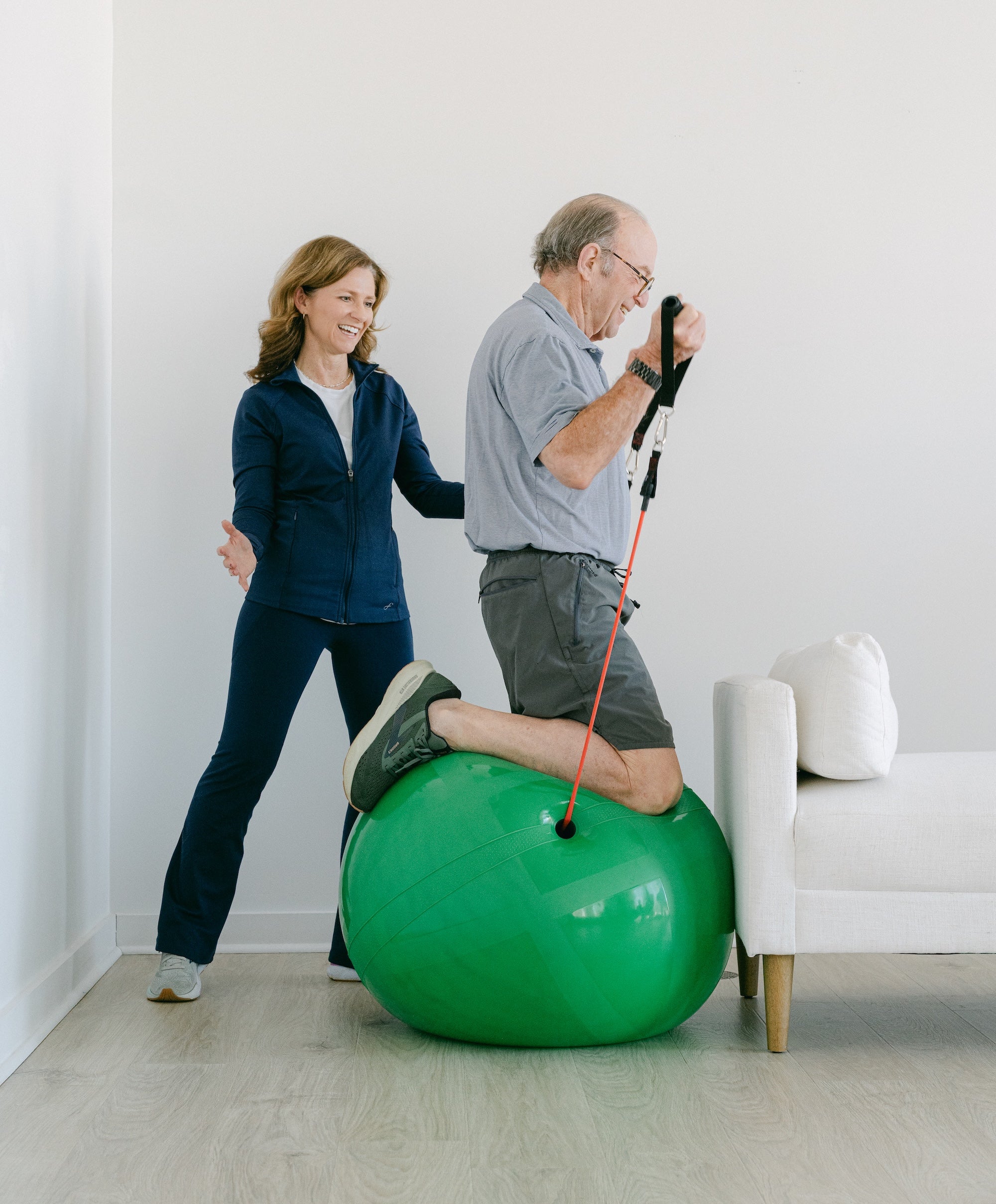 Woman assisting an man on a green exercise ball in a a neutral studio