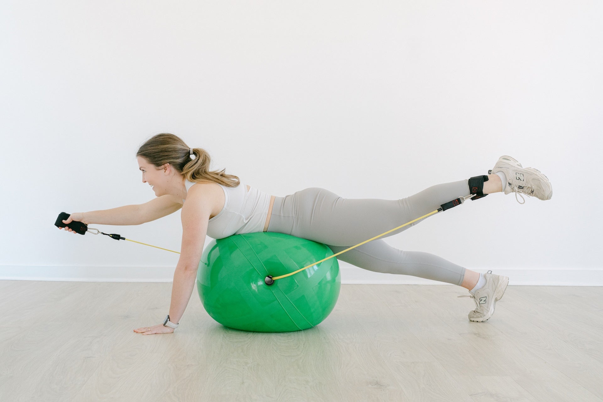 Woman exercising on a green channel ball with resistance bands in a white room